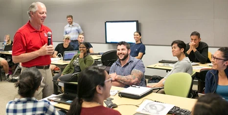 President Robbins speaking with students in a classroom.